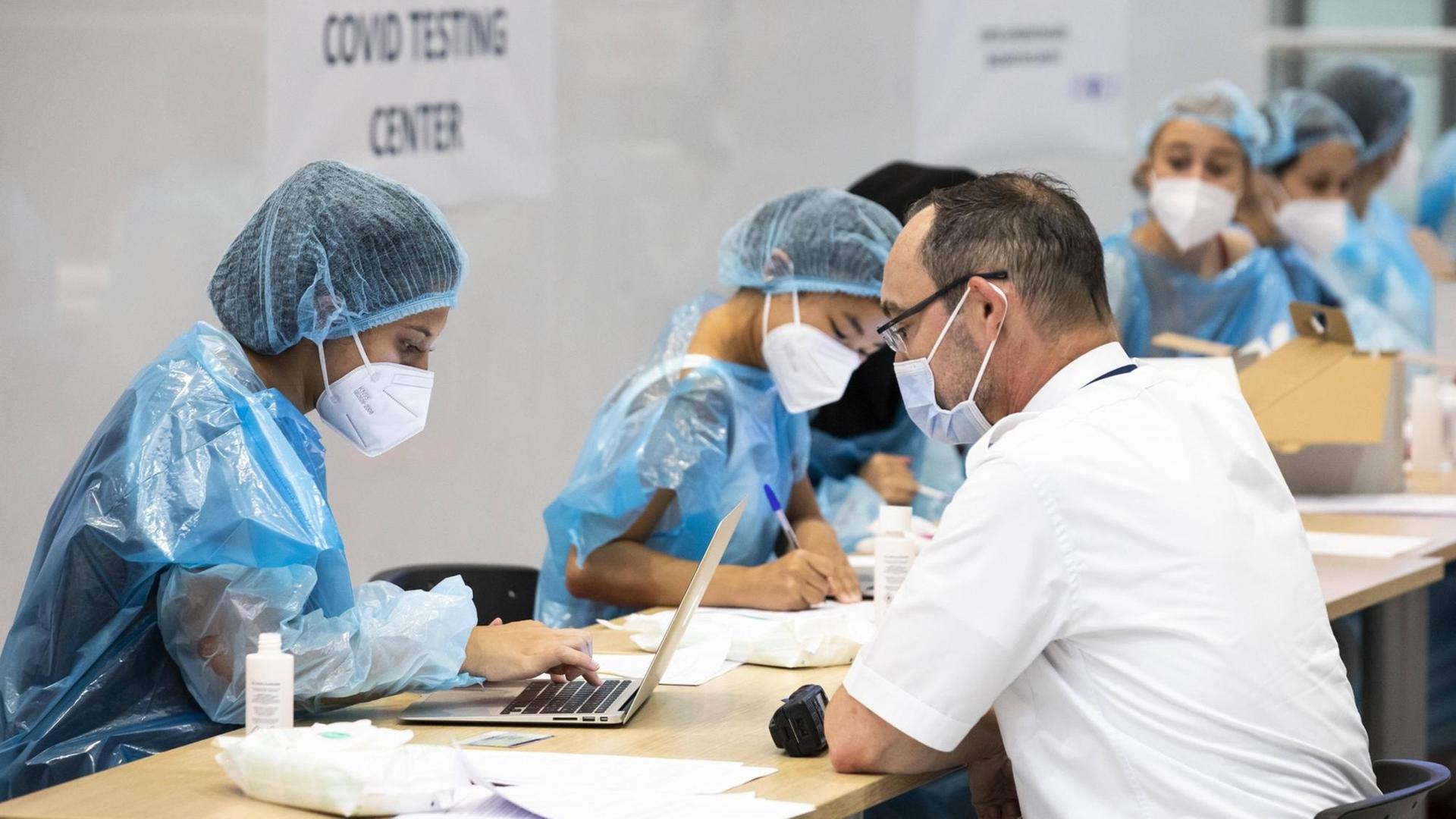 Ein Mann sitzt an einer Coronavirus-Teststation am Charles de Gaulle Flughafen im französischen Roissy mehreren Frauen mit Schutzanzug und -Maske gegenüber. 24. Juli 2020.