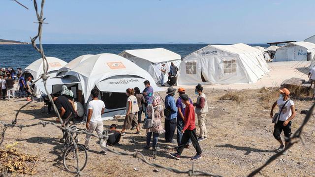 Ein Flüchtlingslager auf der Insel Lesbos in Griechenland. Auf dem Bild sind weiße Zelte und viele Menschen in der Nähe vom Meer.