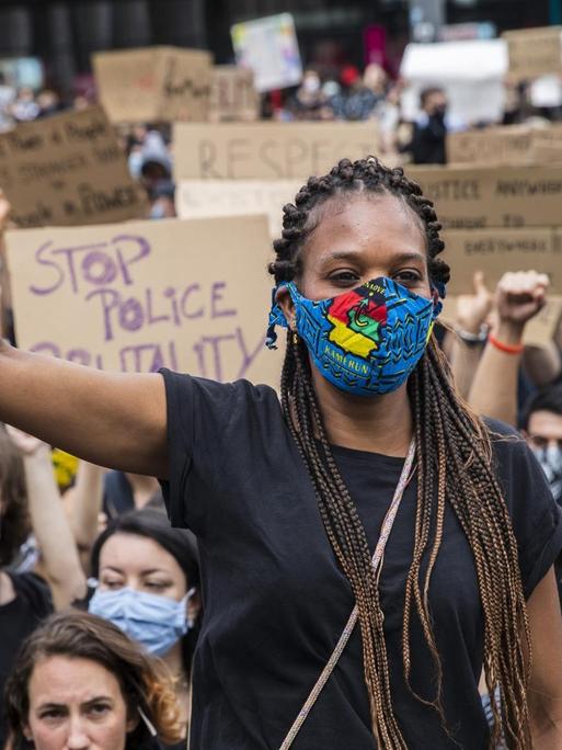 Eine schwarze Frau und viele Demonstranten heben die Faust als Zeichen gegen Rassismus.