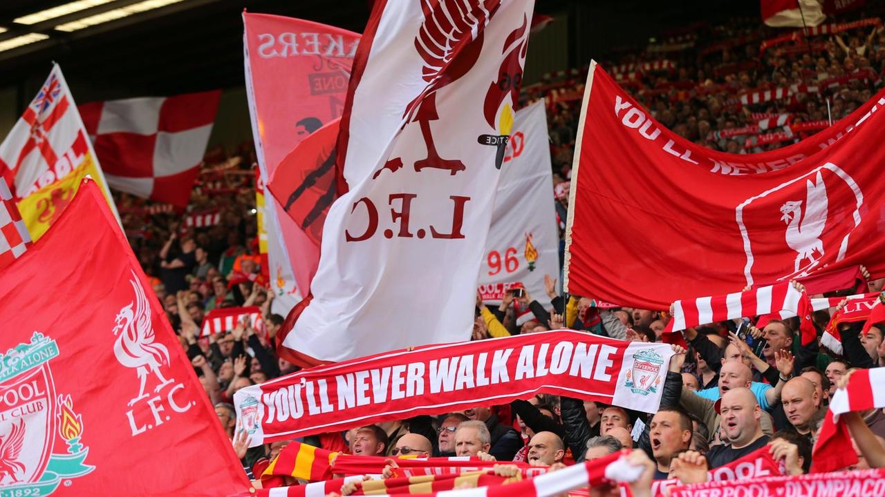 FC Liverpool Fans halten auf den Tribünen im Stadion Flaggen und Vereinsschals in die Höhe mit dem Songtext.