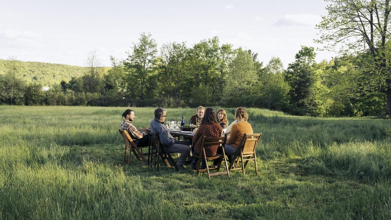 Zusammen genießen eine Gruppe von Freunden ein gemeinsames Essen auf einer grünen Wiese.