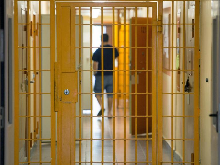 Ein Mann geht am 04.09.2015 in der Justizvollzugsanstalt Hohenleuben in Thüringen hinter einer verschlossenen Gittertür einen Gang entlang.