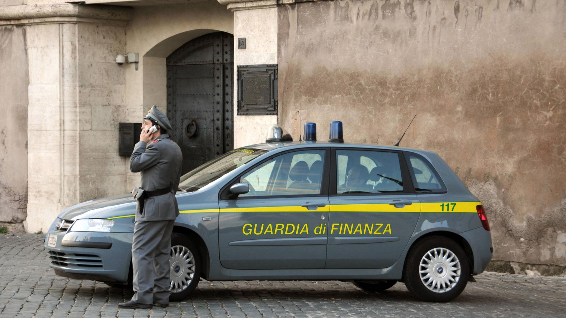 Finanzpolizist steht vor einem Einsatzauto und telefoniert.