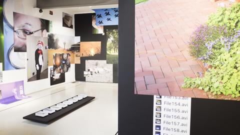 An den Wänden in einem hellen Ausstellungsraum sind unterschiedliche Fotomotive zu einer Collage zusammengefügt.