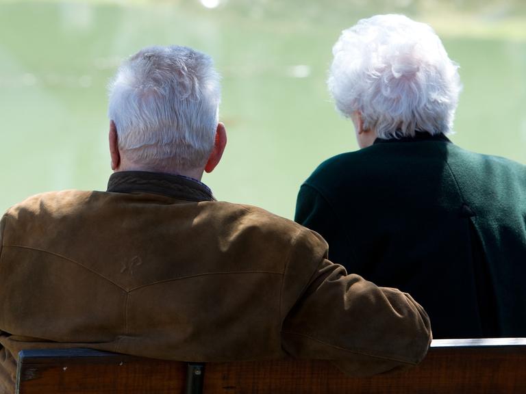 Zwei Senioren sitzen an einem kleinen Teich.