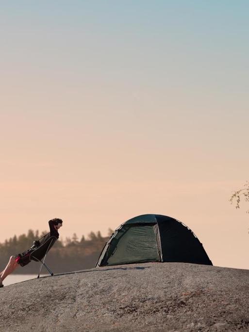 Ein Mann sitzt auf einem Steinhügel am Finnischen Meerbusen und blickt in die Ferne, hinter ihm steht ein kleines Zelt.