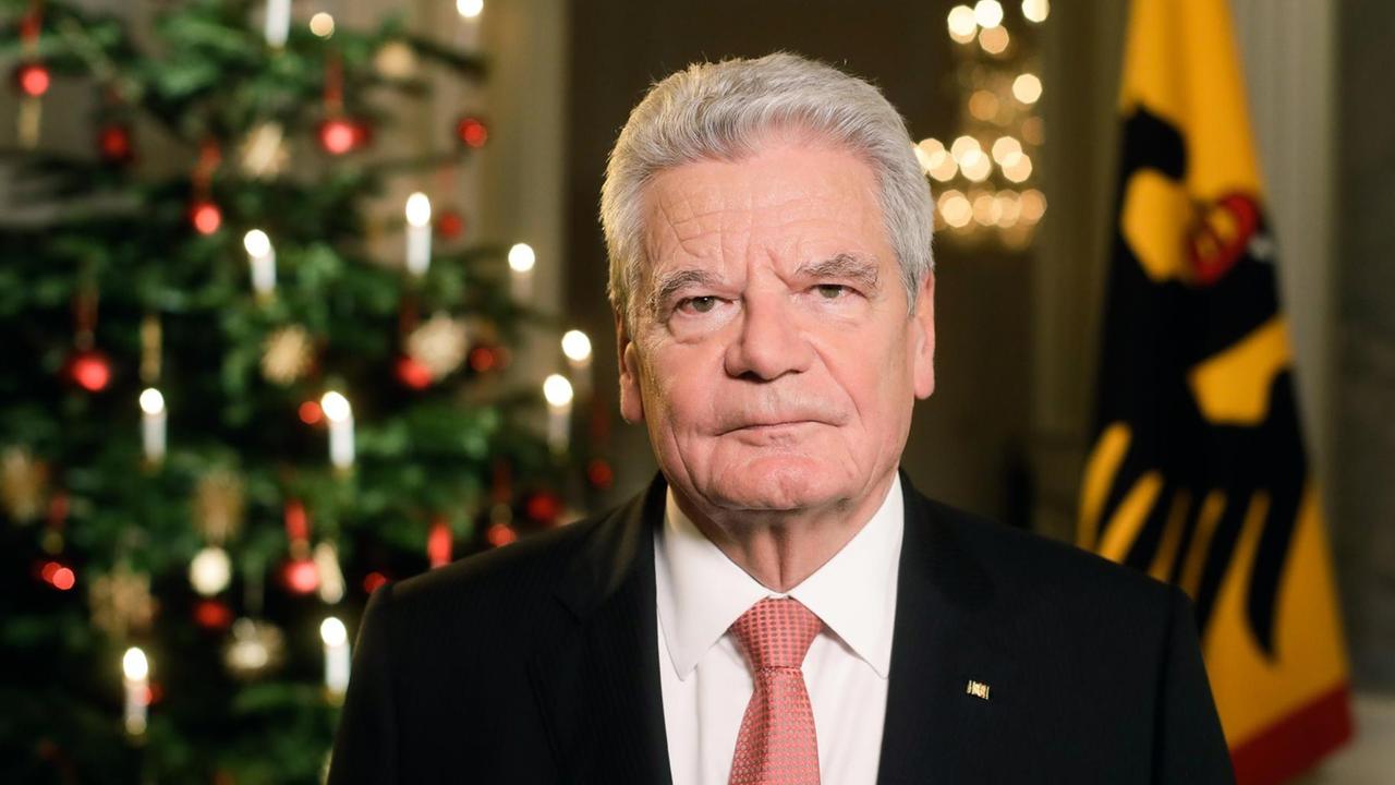 Gauck mit ernstem Blick vor einem Weihnachtsbaum und einer Bundesfahne.