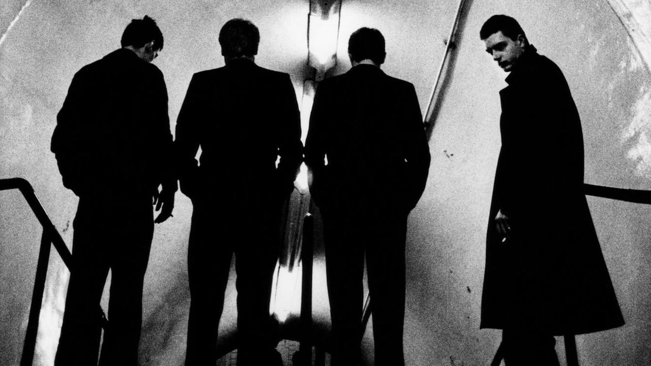 Eine Schwarz-weiß-Aufnahme des Fotografen Anton Corbijn ziegt die Band Joy Division beim Abstieg in die U-Bahn