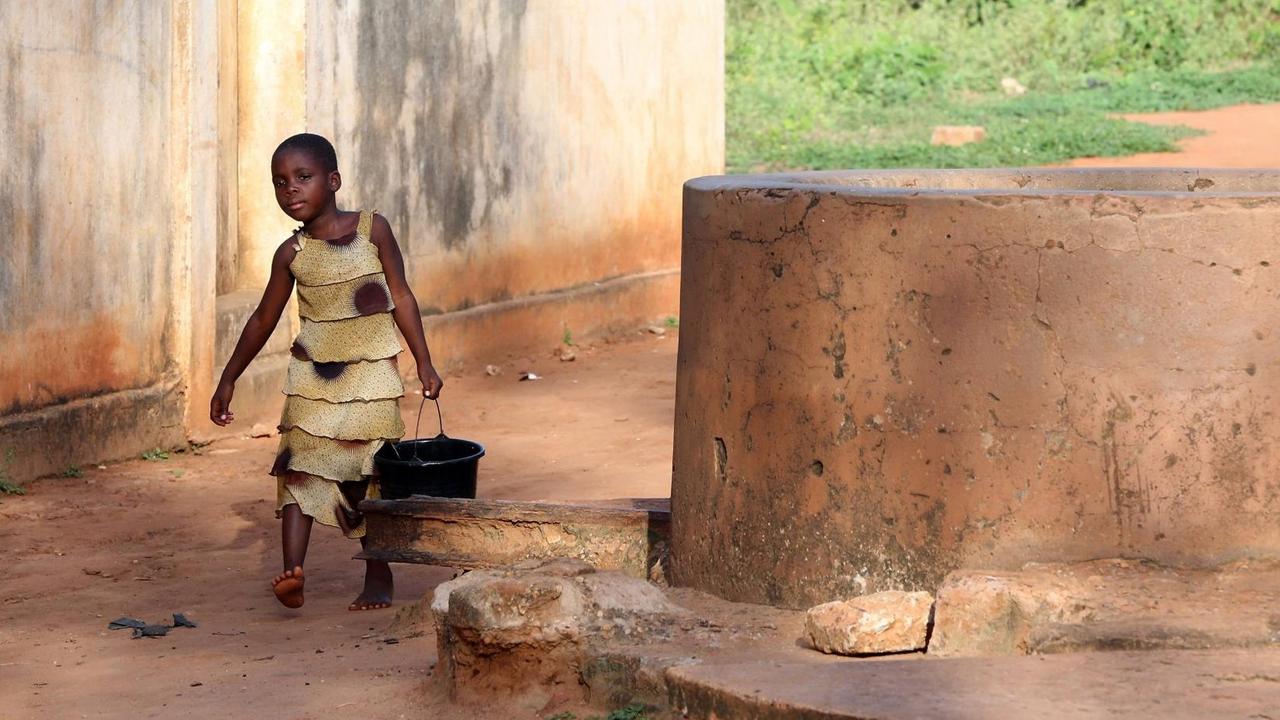 Ein Mädchen trägt einen Wassereimer in einem Dorf in Togo, Afrika. 