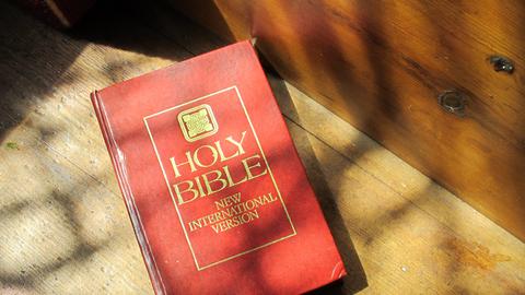 Eine Bibel, Holy Bible, liegt im Schatten von Kirchenfenstern.