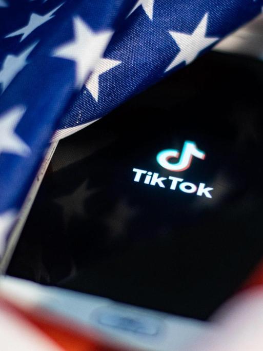 Handy mit TikTok-Logo auf dem Display versinkt in US-Flagge