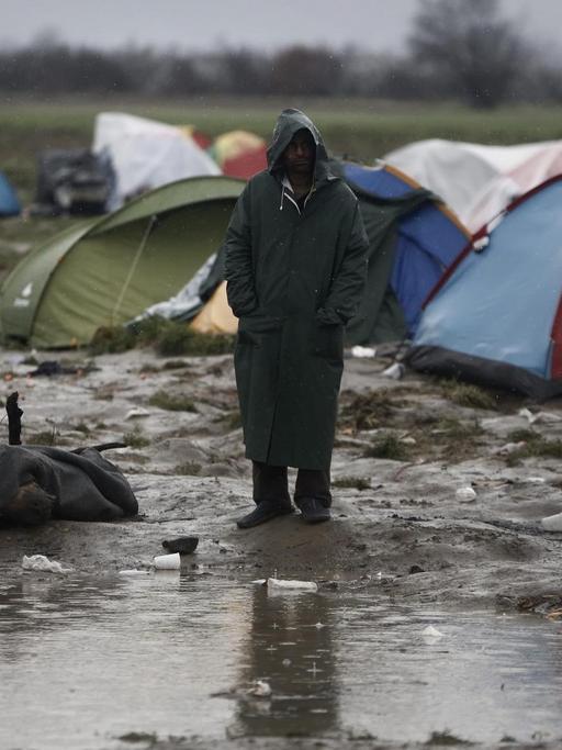 Ein Mann steht vor einer Gruppe von Campingzelten im Regen, vor ihm eine große Pfütze.