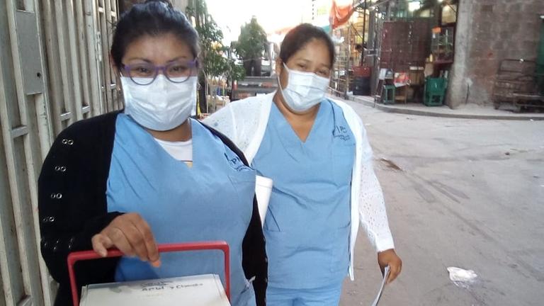 Thelma Soria und eine Kollegin mit Atemschutzmasken und einer Kühlbox in der Hand.