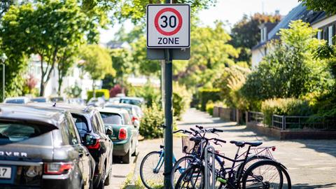 Ein Verkehrsschild zur Geschwindigkeitsbegrenzung auf Tempo 30 steht auf einer Hauptstraße vor geparkten Autos.