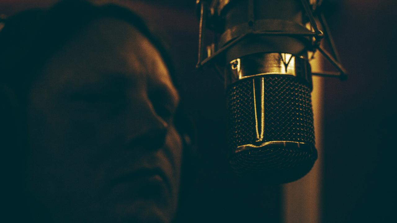Ein Mann steht in einem Tonstudio vor einem Mikrofon.