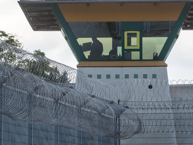 Ein Wachturm in einer Justizvollzugsanstalt hinter einem Zaun mit Stacheldraht.