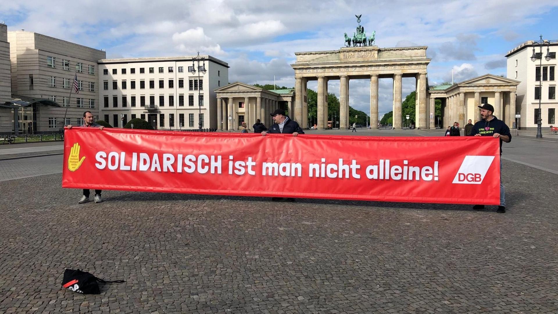 Demonstranten tragen ein Banner mit der Aufschrift "Solidarisch ist man nicht alleine" vom Deutschen Gewerkschaftbund vor dem Brandenburger Tor in Berlin