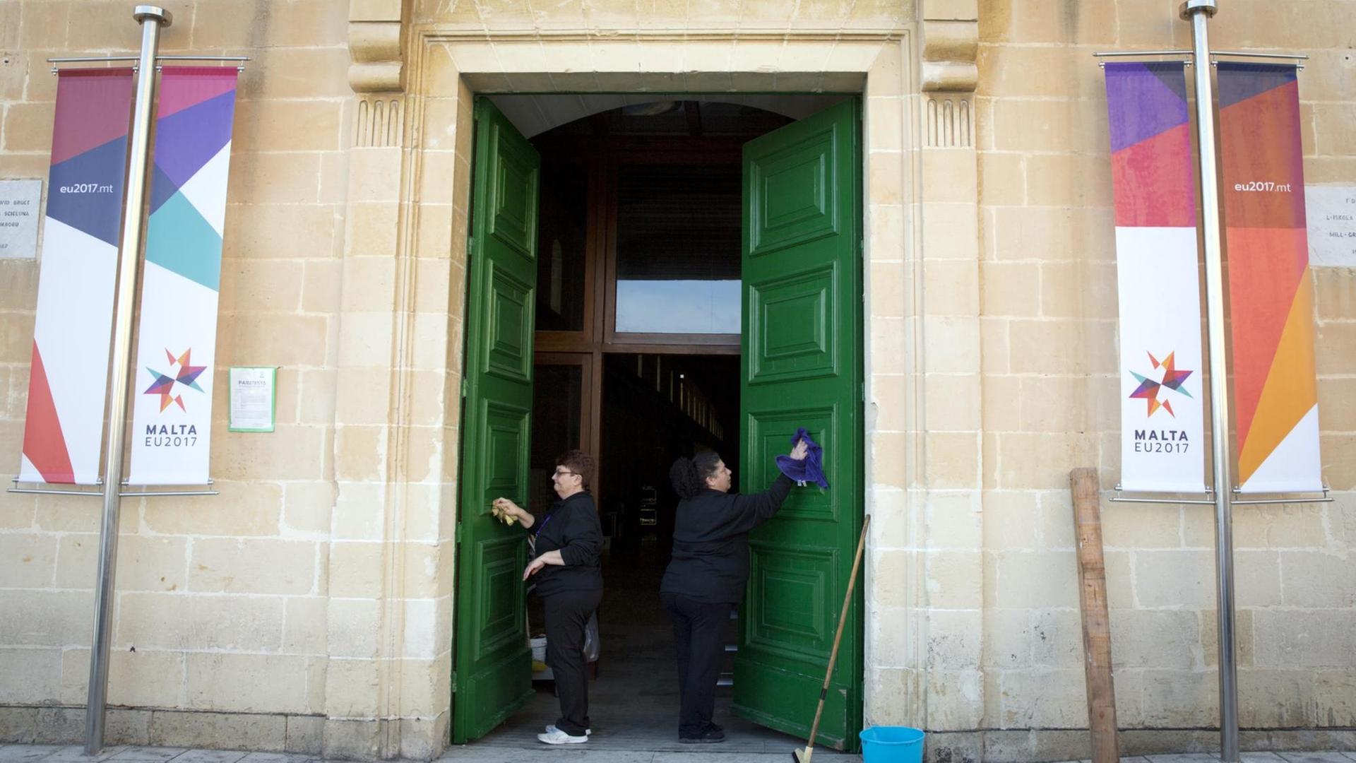 Zwei Frauen reinigen die Tür eines Konferenzzentrums in Malta, in dem sich die Staats- und Regierungschefs der EU zu einem informellen Gipfel treffen.