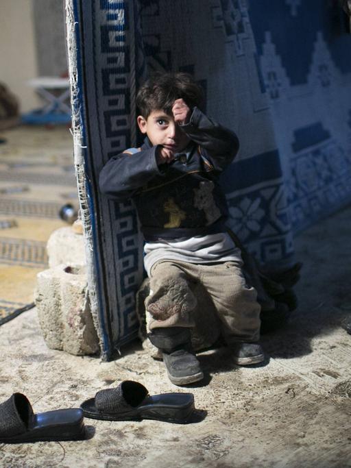 Ein kleiner, ängstlicher, syrischer Junge steht halb in der Knie in einem verlassenen Haus in Aleppo in Syrien. Viele Familien mussten ihr Zuhause verlassen, weil sie entweder in der Nähe von einem militärischen Flugstützpunkt wohnten oder weil ihre Häuser zerbombt wurden.