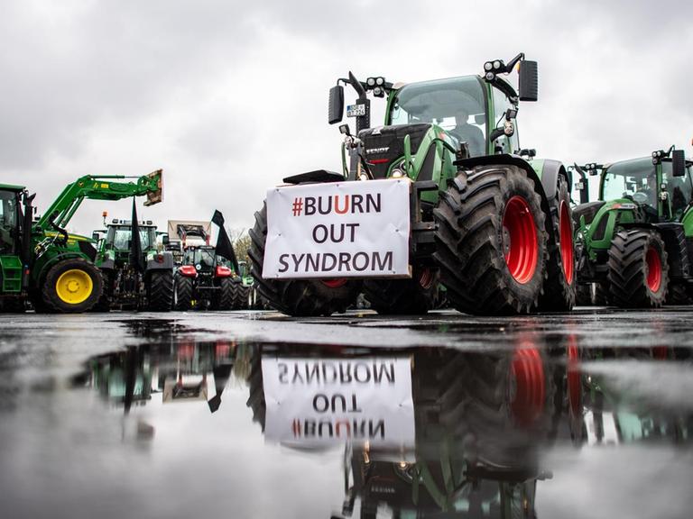 An einem Traktor spiegelt sich in einer Pfütze ein Transparent mit der Aufschrift: "#Buurn out Syndrom".