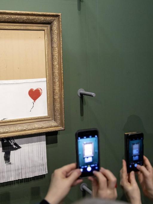 Besucher der Staatsgalerie Stuttgart fotografieren mit ihren Smartphones das teilweise geschredderte Kunstwerk "Love is in the Bin" des Street-Art-Künstlers Banksy.