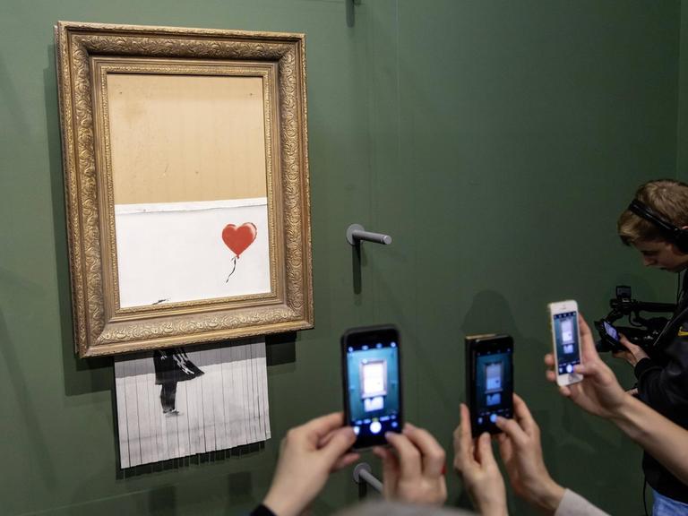 Besucher der Staatsgalerie Stuttgart fotografieren mit ihren Smartphones das teilweise geschredderte Kunstwerk "Love is in the Bin" des Street-Art-Künstlers Banksy.