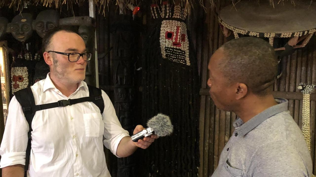 Der Journalist Vladimir Balzer hält dem Direktor des "Blackitude Museums", Christian Nana Tschuisseu, ein Mikrofon zum Interview entgegen.