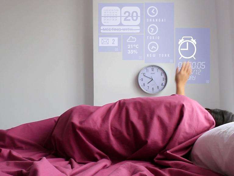 Eine Frau liegt in einem Bett und verändert mit einer Handbewegung das Licht. Die Technik wird in dem Prototyp eines Smart Home in Fuenterrabia in Spanien.