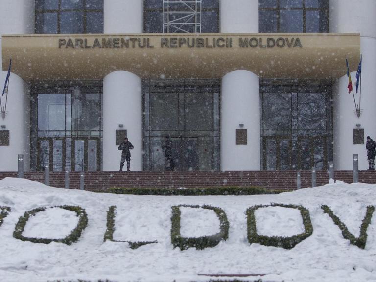 Wachmänner stehen vor dem Parlament in Chisinau, der Hauptstadt der ehemaligen Sowjetrepublik Moldau. Im Vordergrund ein in Stein gehauener Schriftzug Moldova, der teils von Schnee bedeckt ist.