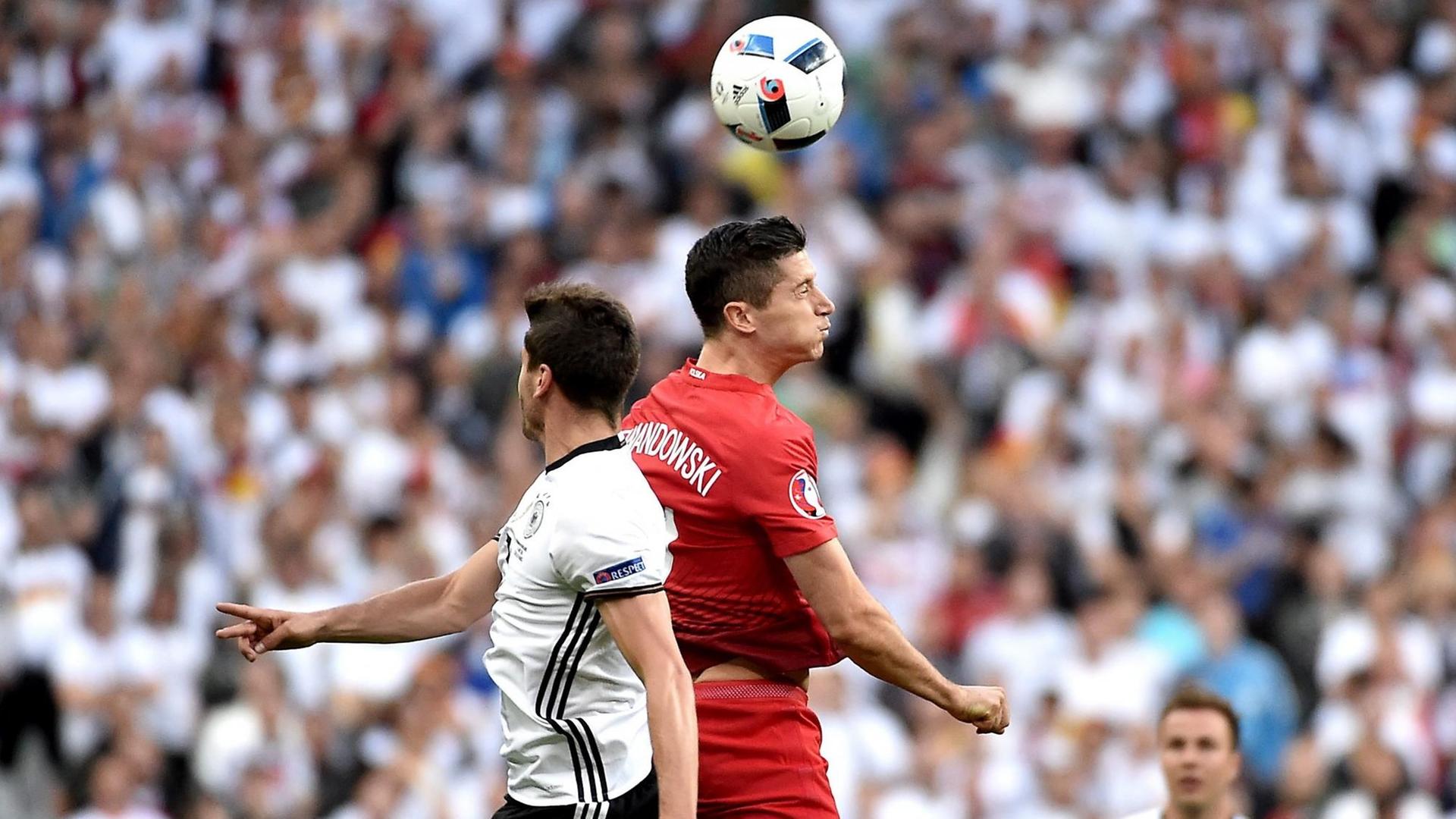 Der polnische National-Spieler Robert Lewandowski und der deutsche National-Spieler Jonas Hector springen nach dem Ball.