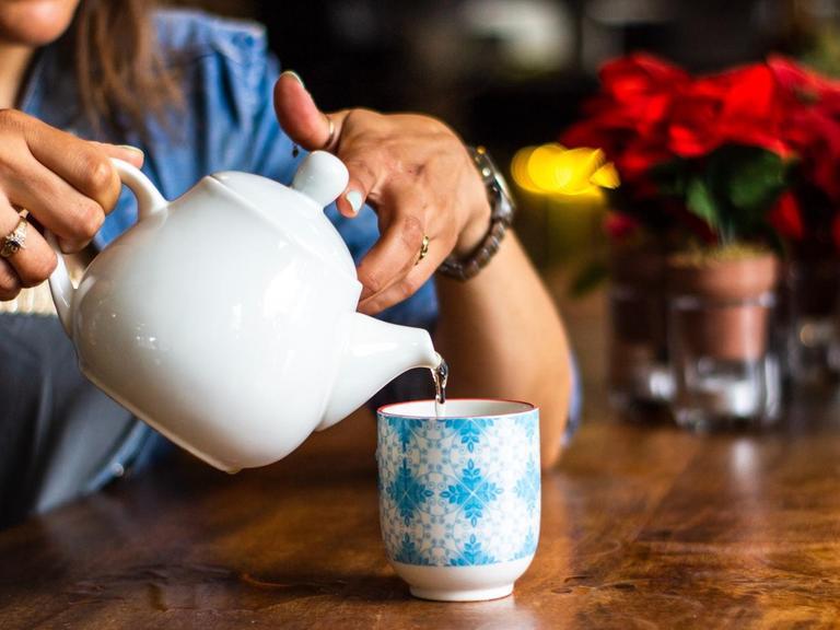 Eine Frau schenkt sich Teewasse in eine Tasse ein.