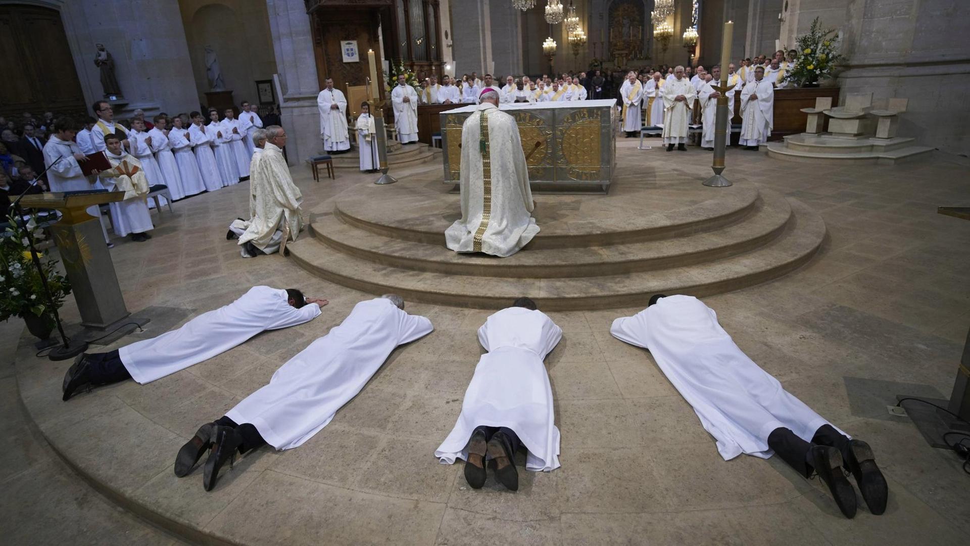 Vier Männer in weißen Gewändern liegen ausgestreckt aus dem Boden, im Hintergrund befinden sich der Altar und weitere Männer.