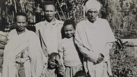 Die Schwarzweißfotografie zeigt eine schwarze Familie. Zu sehen sind Mutter, Vater (mit weißer Kopfbedeckung) und drei Söhne.