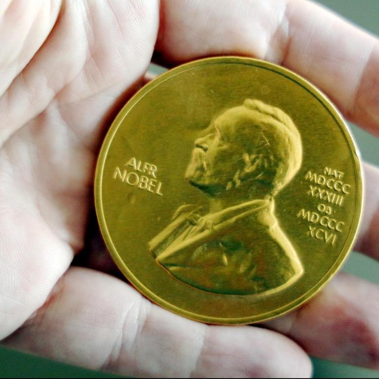 In einer Hand liegt eine goldene Nobelpreis-Medaille.