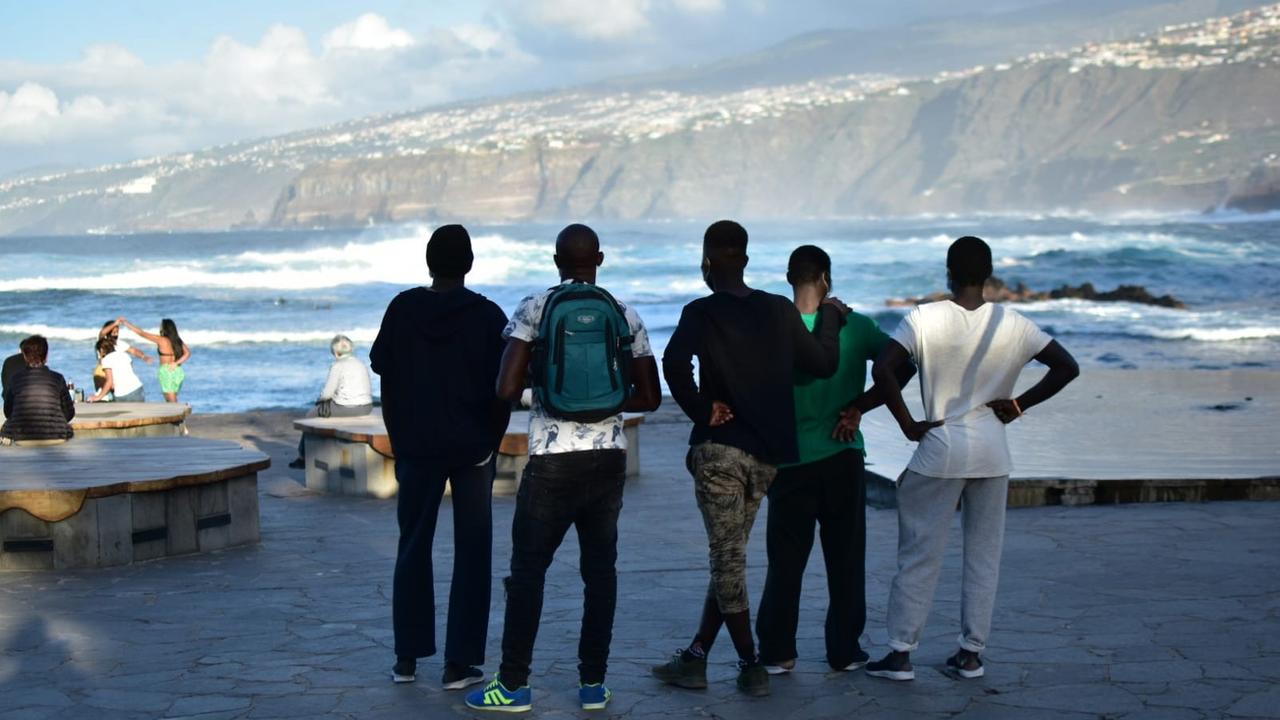 Fünf junge Schwarzafrikaner stehen mit dem Rücken zur Kamera an der Küste und schauen ins Meer.