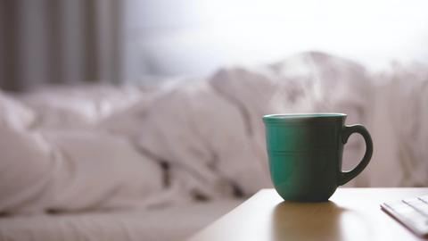 Eine Tasse mit heißem Getränk steht auf einem Tisch neben einem ungemachten Bett.