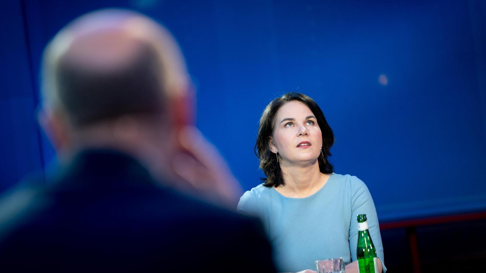 Die grüne Kanzlerkandidatin Annalena Baerbock steht an einem Tisch und schaut nach oben, im Vordergrund unscharf und von hinten Olaf Scholz, Kanzlerkandidat der SPD.