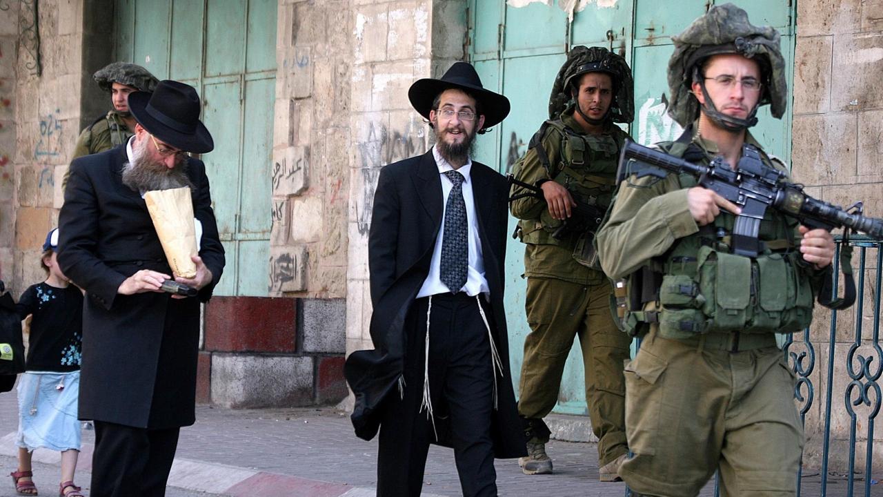 Israelische Siedler laufen bewacht von Soldaten durch eine Straße in Hebron, die nur ihnen zugänglich ist. 