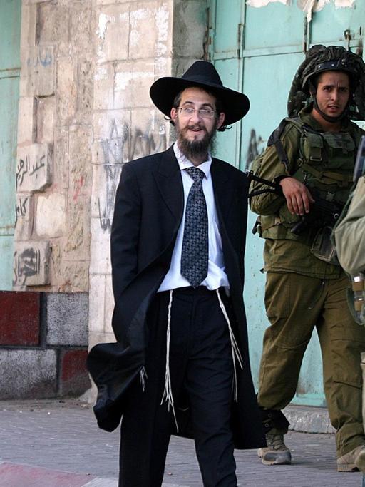 Israelische Siedler laufen bewacht von Soldaten durch eine Straße in Hebron, die nur ihnen zugänglich ist.