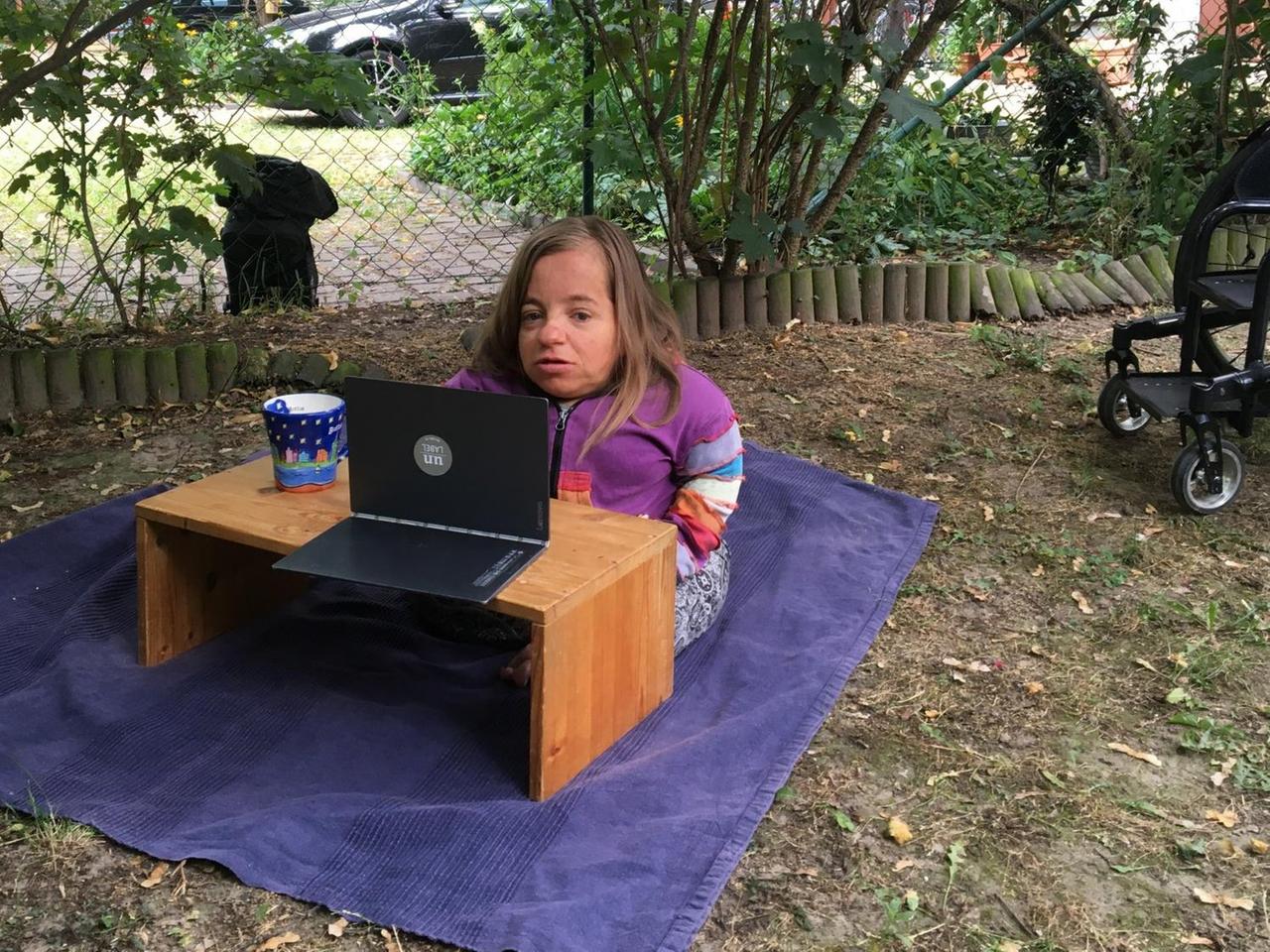 Jana Zöll bei der Onlineprobe - draußen damit unser Autor dabei sein kann. Sie sitzt auf einer blauen Decke, vor ihr auf einem Tisch steht ein Laptop.