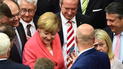 Bundeskanzlerin Angela Merkel (CDU) legt während der Abstimmung zu Verhandlungen über ein neues Griechenland-Hilfspaket ihren Stimmzettel in die Urne. Sie wird dabei von weiteren Bundestagsabgeordneten umringt, darunter Vizekanzler Sigmar Gabriel (SPD).