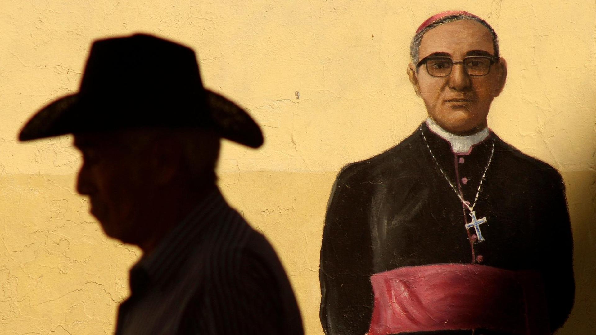 Der Schatten eines Mannes mit Hut auf einem Wandgemälde, das den ermordeten Erzbischof Oscar Arnulfo Romero darstellt.