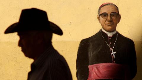 Der Schatten eines Mannes mit Hut auf einem Wandgemälde, das den ermordeten Erzbischof Oscar Arnulfo Romero darstellt.