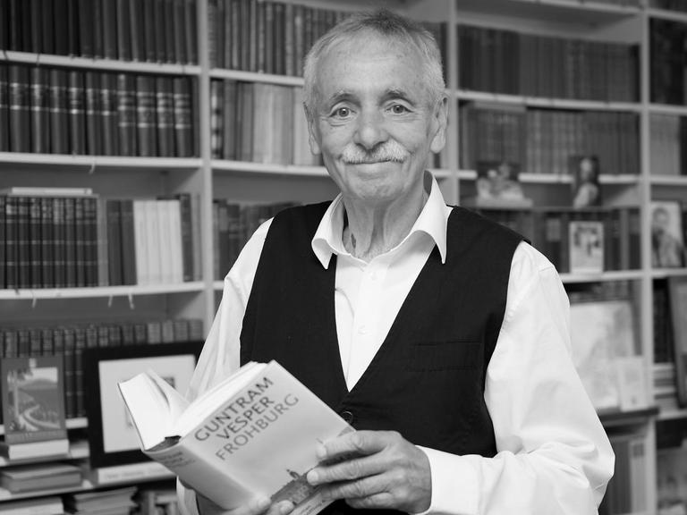 Der Schriftsteller Guntram Vesper steht vor einem Bücherregal und hält ein Buch in der Hand