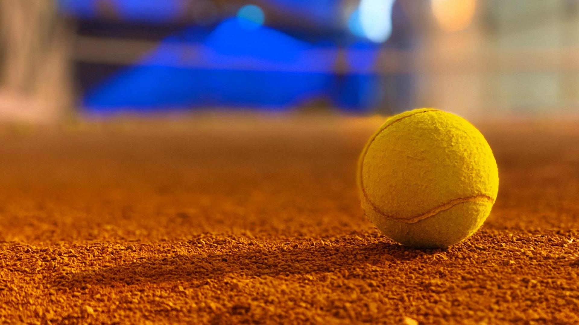 Großaufnahme eines gelben Tennisballs auf orange-braunem Grund