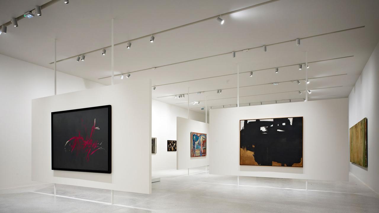 Ein Ausstellungsraum mit Stellwänden, an denen moderne Gemälde zu sehen sind