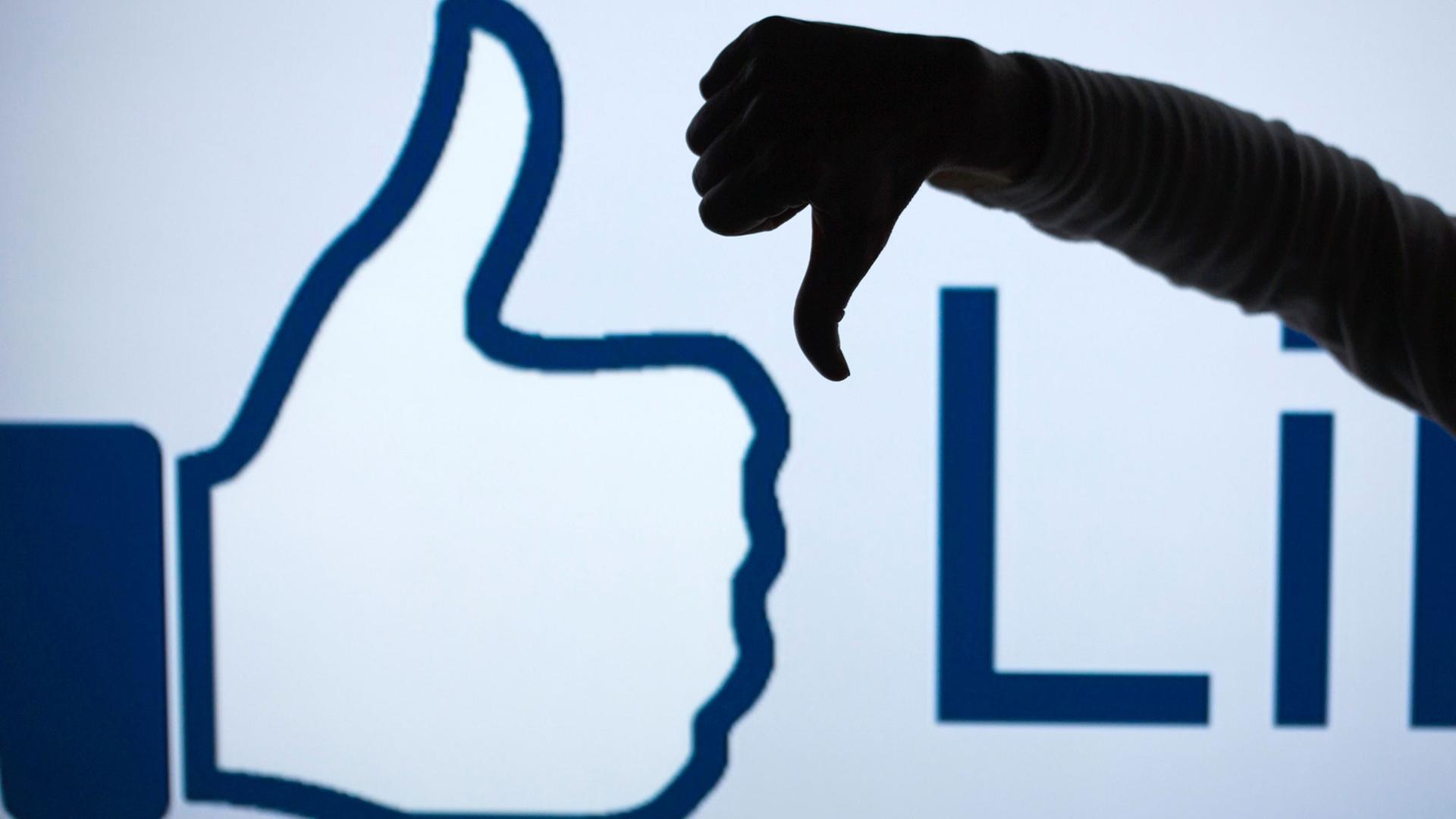 Ein Mann zeigt vor dem vergrößerten Like-Symbol der Facebook-Seite mit seinem Daumen nach unten (gestelltes Foto).