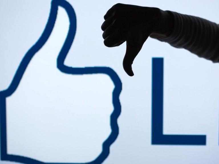 Ein Mann zeigt vor dem vergrößerten Like-Symbol der Facebook-Seite mit seinem Daumen nach unten (gestelltes Foto).