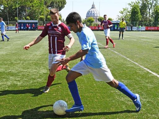 Ein Spieler des Teams Mater Ecclesiae aus Vatikanstadt kontrolliert den Ball beim Clericus Cup 2016 i n Rom. Im Hintergrund ist der Petersdom zu sehen.