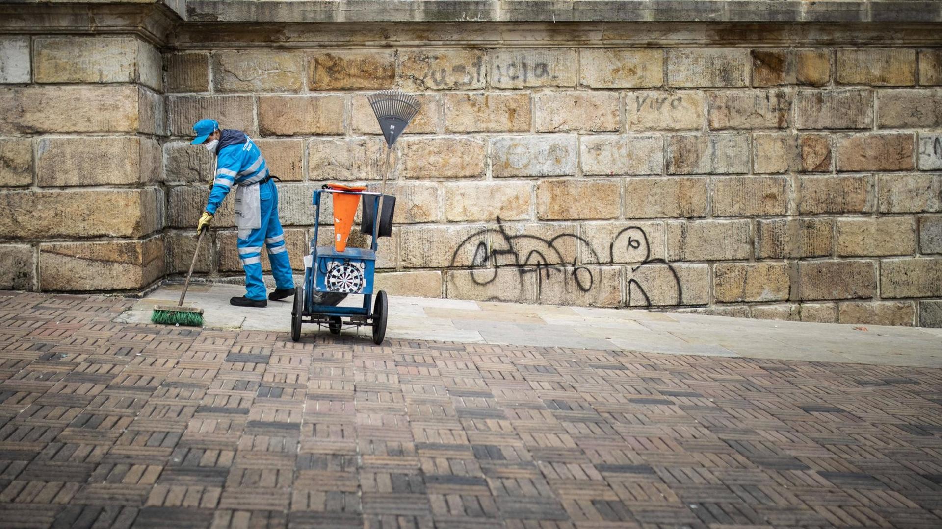 Eine Reinigungskraft in einem Blaumann schrubbt Pflaster vor einem Steingebäude
